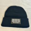 Close-up image of the black “We Will Resist” rolled beanie by Slash-32, showing the grey rectangle patch with binary matrix and “We Will Resist” text.