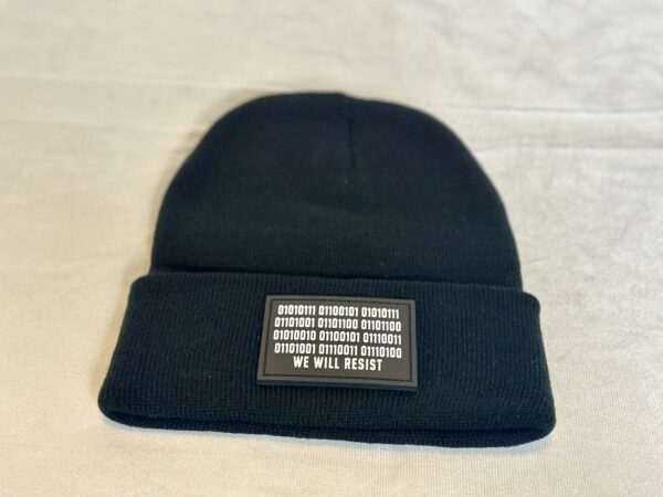 Close-up image of the black “We Will Resist” rolled beanie by Slash-32, showing the grey rectangle patch with binary matrix and “We Will Resist” text.