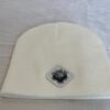 Image of white skull cap style fitted beanie with diamond-shaped white patch featuring microchip symbol and “/32” text, sewn onto front of hat.