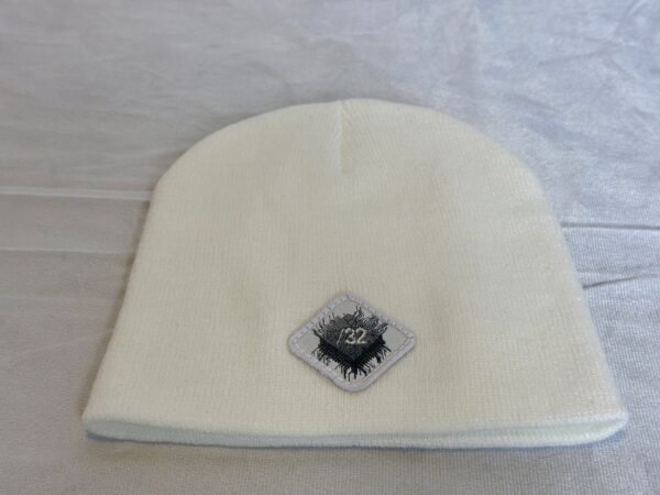 Image of white skull cap style fitted beanie with diamond-shaped white patch featuring microchip symbol and “/32” text, sewn onto front of hat.