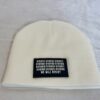 Image of white skull cap style fitted beanie with rectangular black patch featuring binary code above “We Will Resist” text, sewn onto front of hat.
