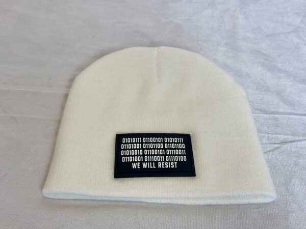Image of white skull cap style fitted beanie with rectangular black patch featuring binary code above “We Will Resist” text, sewn onto front of hat.