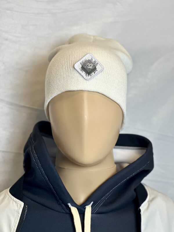 Image of white slouch style fitted beanie on mannequin with diamond-shaped white patch featuring microchip symbol and “/32” text, sewn onto front of hat.