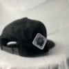 Side-back view of the Slash-32 9/50 Snapback hat, Black (Panda Mode) "We Will Resist" cap, featuring a white diamond-shaped patch with the /32 microchip emblem stitched in.