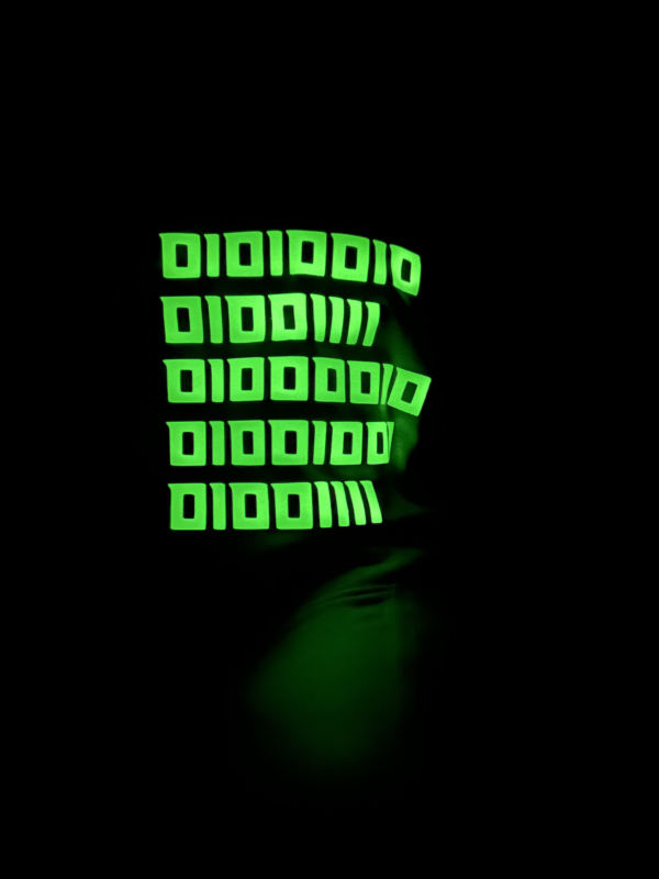 Image of the black FH0 – Knøwn H0st’s Binary Hoodie by Slash-32 showing the custom binary signature glowing in the dark on the hood.