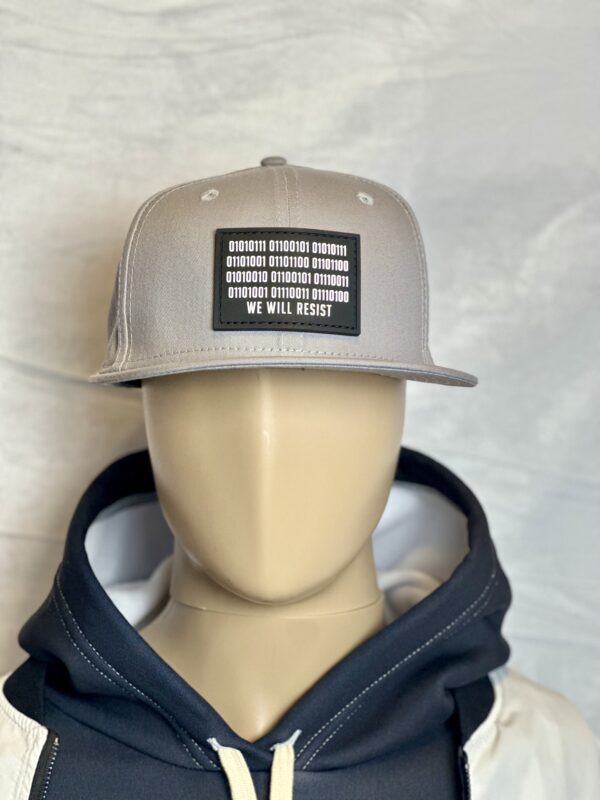 Image of mannequin wearing the Slash-32 9/50 Snapback hat, Grey "We Will Resist" cap with hoodie, showing the front patch with binary and “We Will Resist” text.