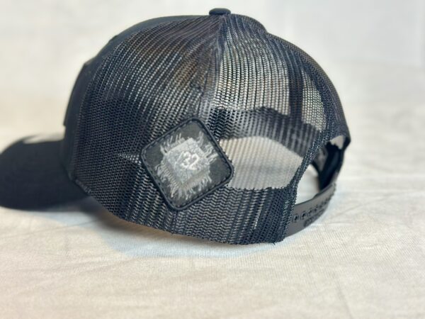 Close-up image of the back of the Slash-32 Trucker Style Snapback hat - Black "We Will Resist" cap, highlighting the diamond-shaped /32 microchip patch on the side.