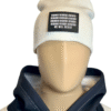 Image of white slouch style fitted beanie on mannequin with rectangular black patch featuring binary code above “We Will Resist” text, sewn onto front of hat.