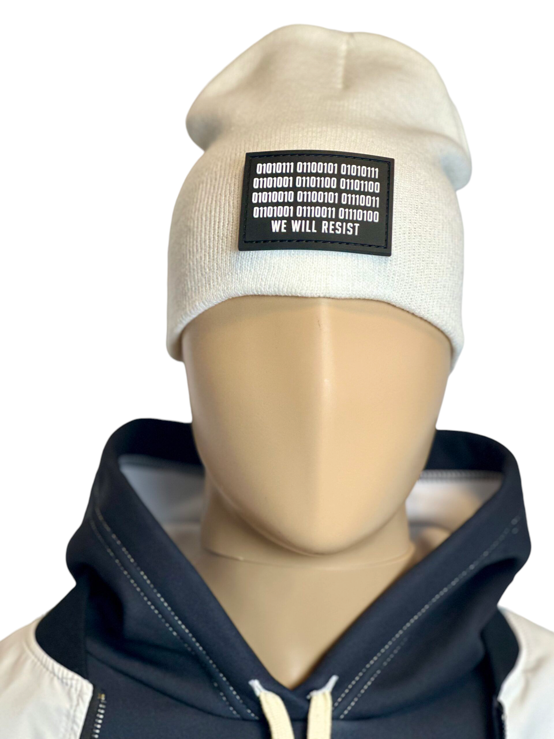 Image of white slouch style fitted beanie on mannequin with rectangular black patch featuring binary code above “We Will Resist” text, sewn onto front of hat.