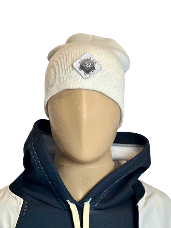 Image of white slouch style fitted beanie on mannequin with diamond-shaped white patch featuring microchip symbol and “/32” text, sewn onto front of hat.