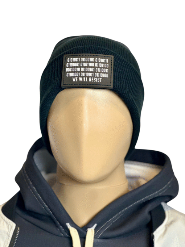 Image of the black “We Will Resist” rolled beanie by Slash-32 on a mannequin wearing a hoodie, featuring a grey rectangle patch with binary matrix and “We Will Resist” text.