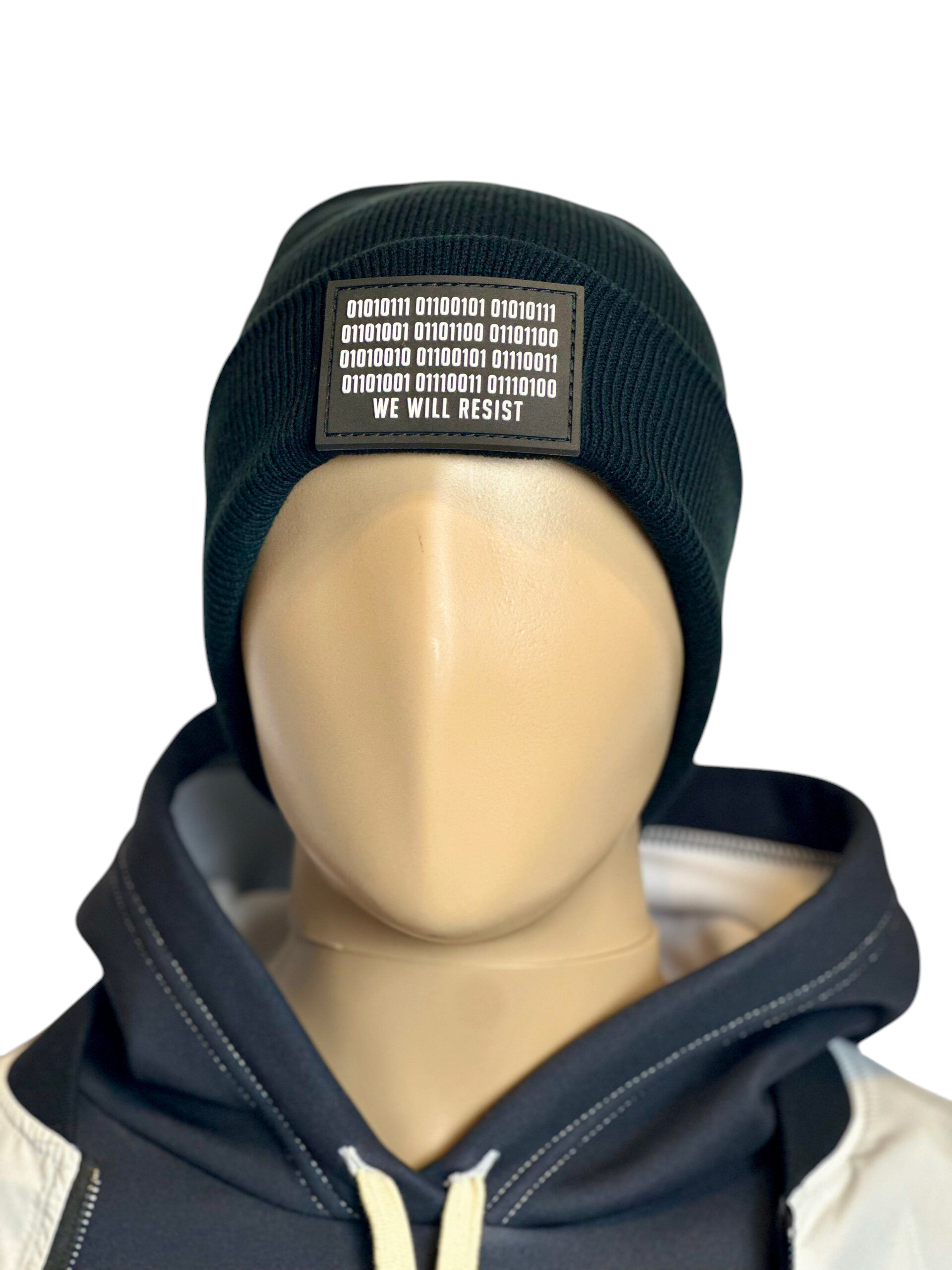 Image of the black “We Will Resist” rolled beanie by Slash-32 on a mannequin wearing a hoodie, featuring a grey rectangle patch with binary matrix and “We Will Resist” text.