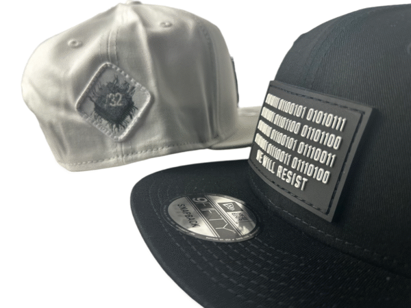 Image featuring a black Slash-32 9/50 Snapback hat with a black binary patch and a white fitted hat with a white diamond patch, both showcasing the /32 microchip emblem.