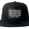 Front view of the Slash-32 9/50 Snapback hat, Black (Panda Mode) "We Will Resist" cap, displaying a black rectangle patch with binary code above the “We Will Resist” text.