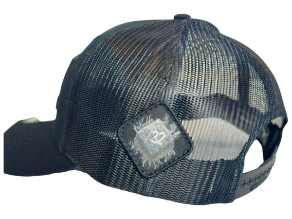 Close-up image of the back of the Slash-32 Trucker Style Snapback hat - Black "We Will Resist" cap, highlighting the diamond-shaped /32 microchip patch on the side.