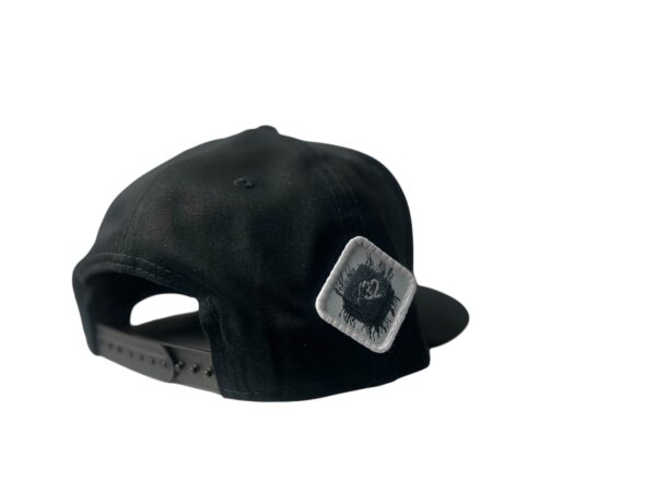 Side-back view of the Slash-32 9/50 Snapback hat, Black (Panda Mode) "We Will Resist" cap, featuring a white diamond-shaped patch with the /32 microchip emblem stitched in.
